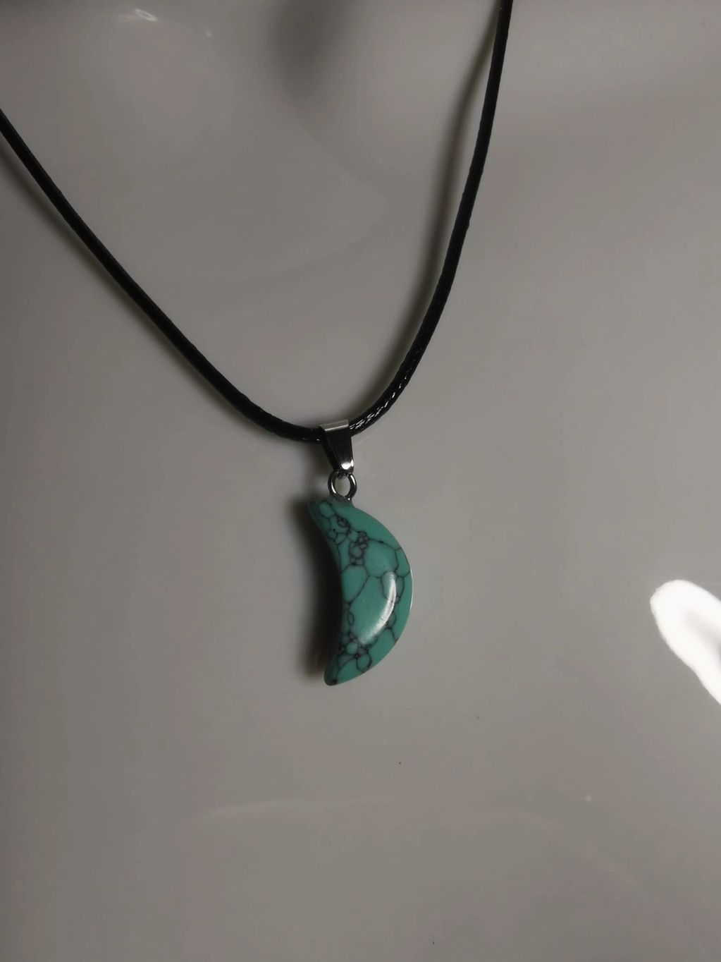Turquoise crescent moon pendant on black cord.