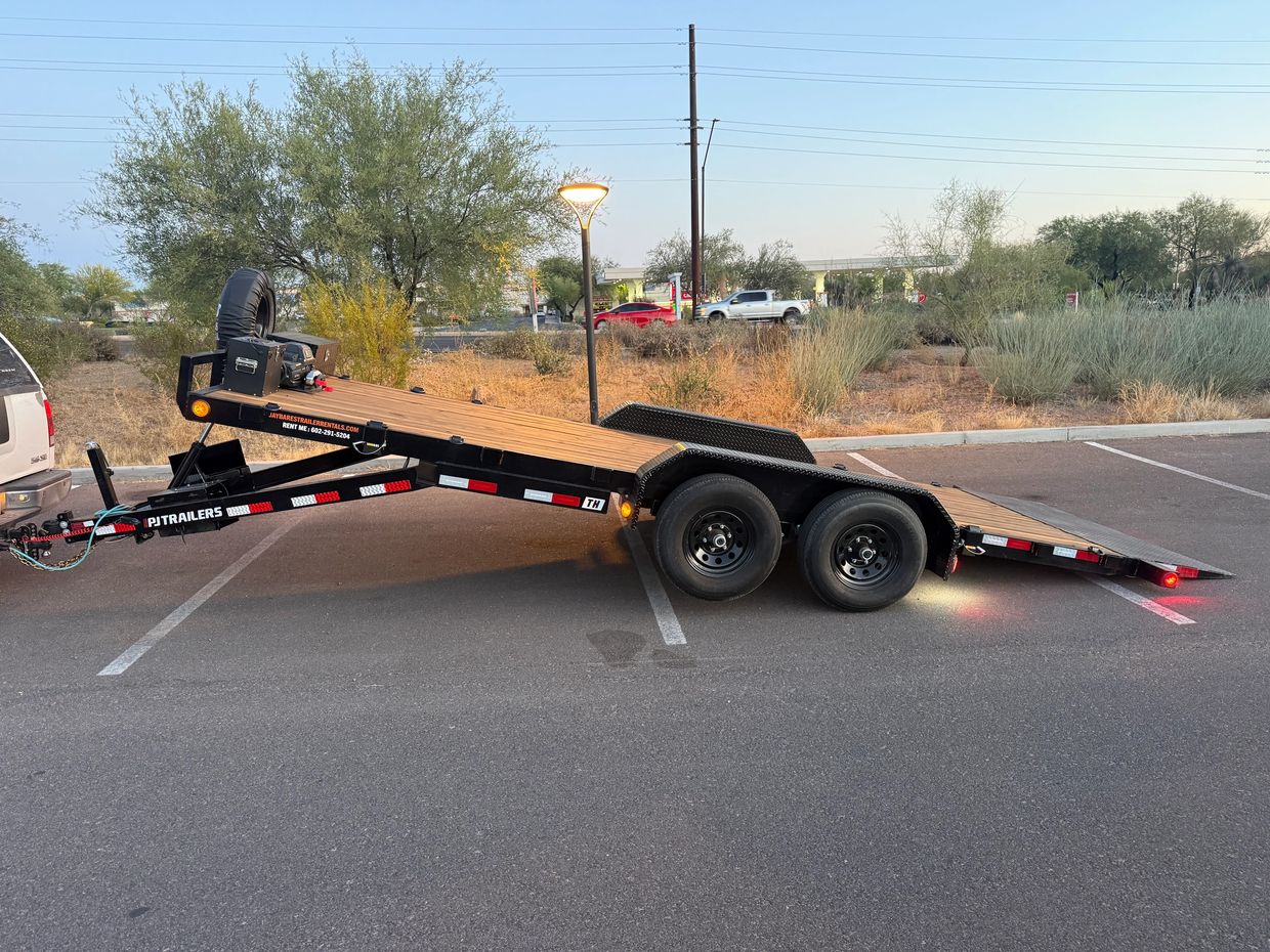 A tilt trailer attached to a vehicle in a parking lot at dusk.