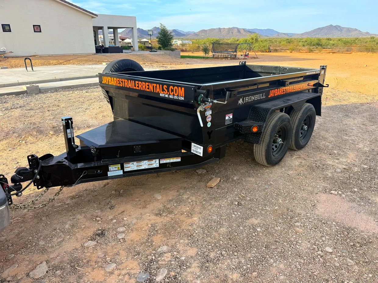 Black rental trailer parked on a dirt lot with mountains in the background.