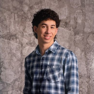 Young man in a blue plaid shirt posing against a textured backdrop.
