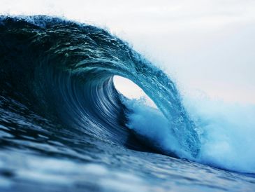 A powerful ocean wave curling with white foam under a cloudy sky.