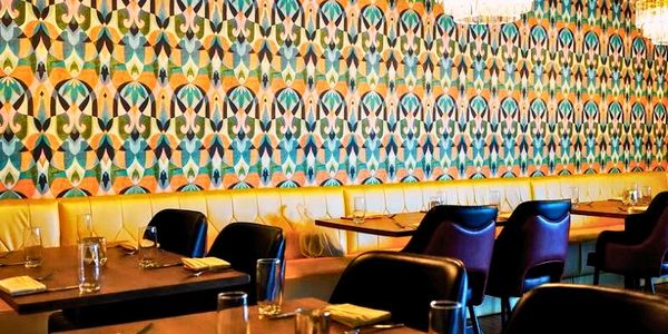 Elegant restaurant interior with colorful geometric wallpaper and chandeliers.