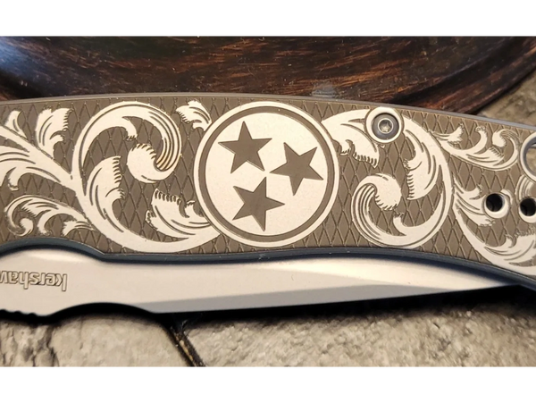 Engraved Kershaw folding knife with intricate floral patterns and three stars emblem.
