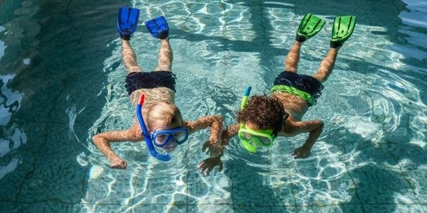 Two kids snorkeling in a pool with flippers.