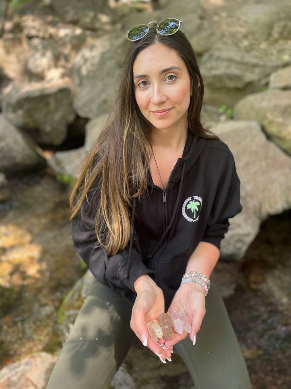 Woman outdoors holding several crystals in her hands, smiling gently.