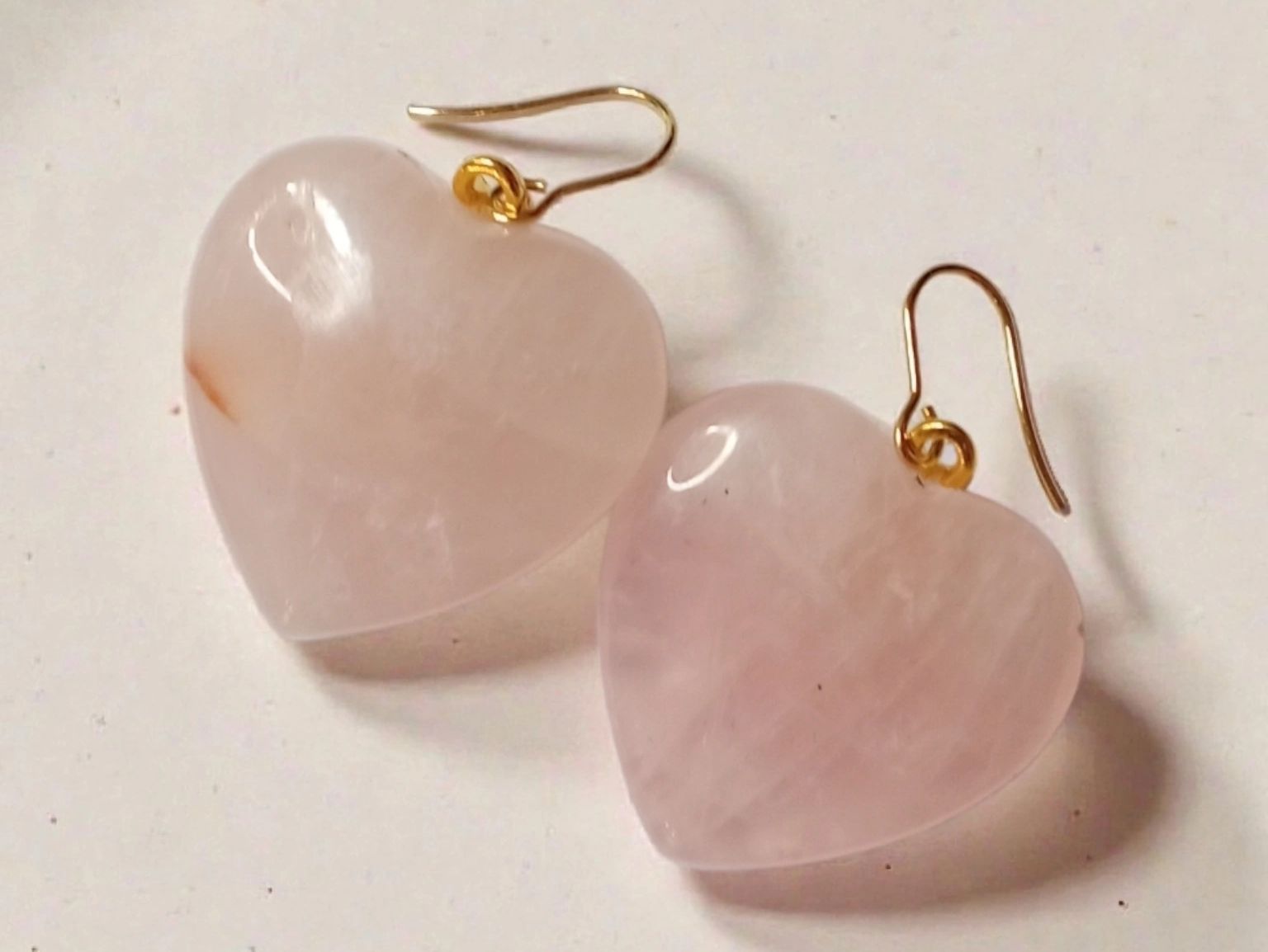 A pair of rose quartz heart shaped crystals on gold earring hooks.
