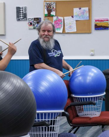 Elderly man enjoying drumming on exercise balls in a cheerful setting.