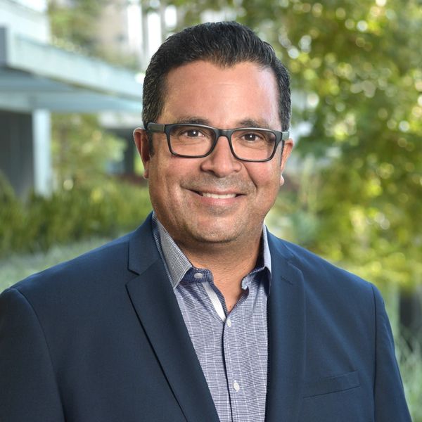 Smiling man in glasses and business attire outdoors.