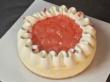 A cheesecake topped with whipped cream and strawberry jelly.