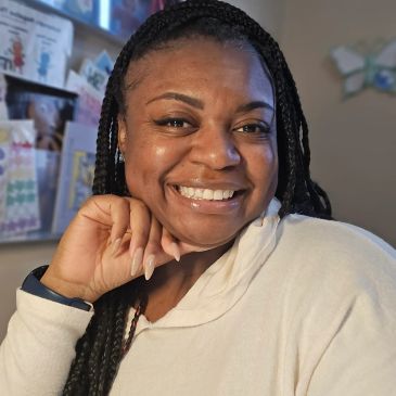 Smiling woman with braided hair and a white hoodie.