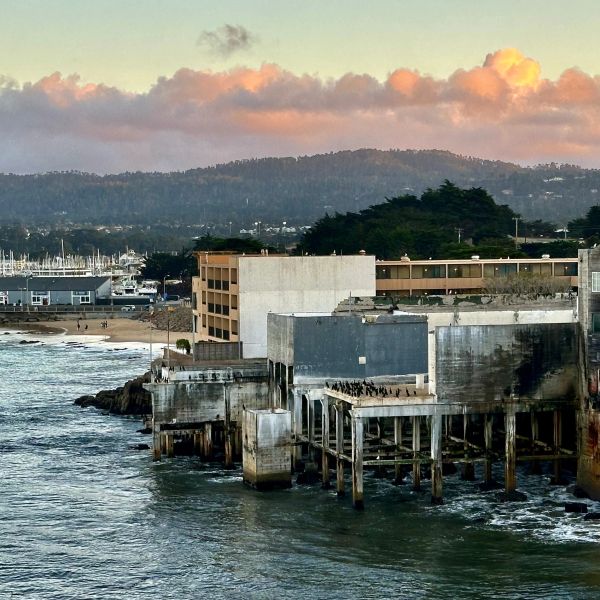 Old buildings on a waterfront with hills and sunset clouds.