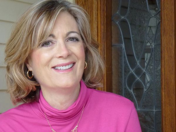 Smiling woman in a pink top by a decorative glass door.