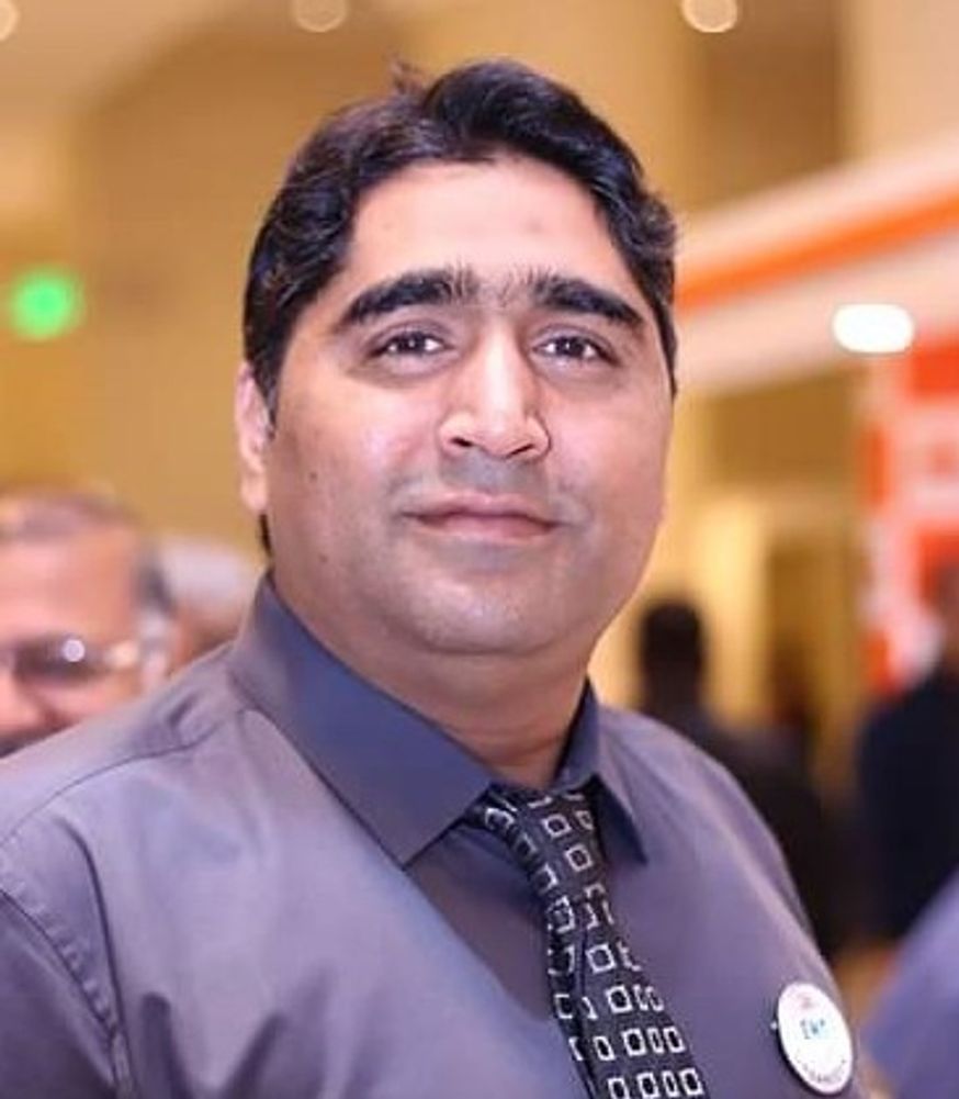 Man in a gray shirt and patterned tie at an indoor event.