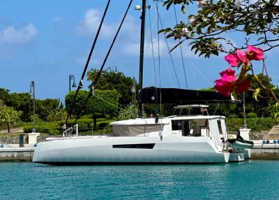A sleek white sailboat docked by calm waters with flowers in the foreground.