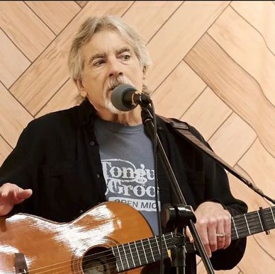 An older man singing and playing guitar with a microphone.