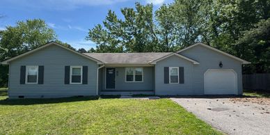 Single-story gray house with a garage and green lawn on a sunny day.