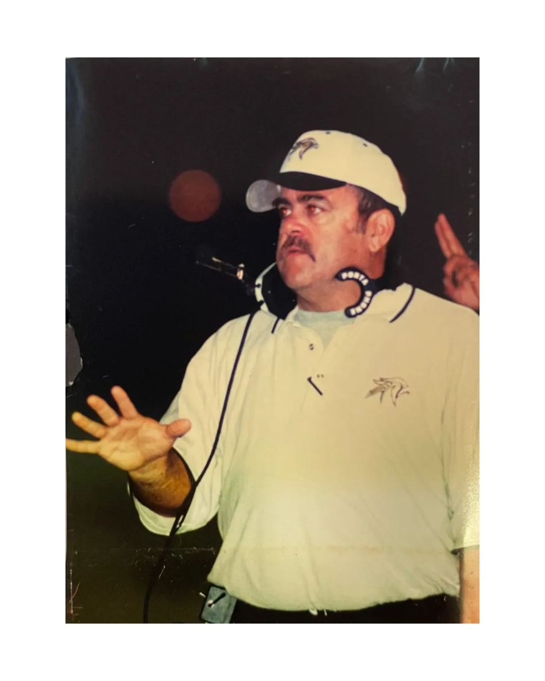 Coach in white shirt and cap giving instructions with headset around neck.
