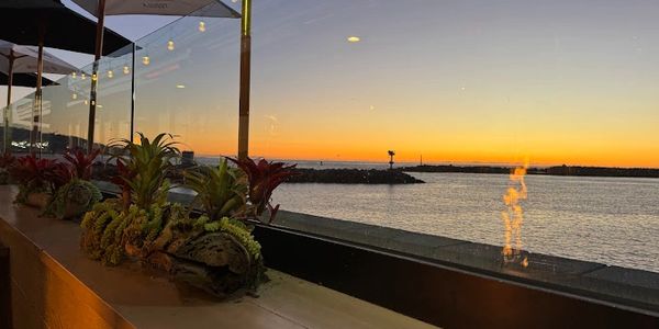 Sunset view over water with plants and glass barrier at a waterfront seating area.