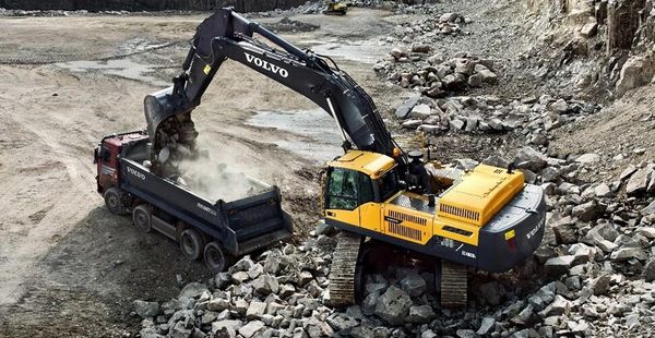 A Volvo excavator loading rocks into a dump truck at a quarry.