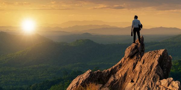 Man standing on a rocky peak watching the sunset over mountains.