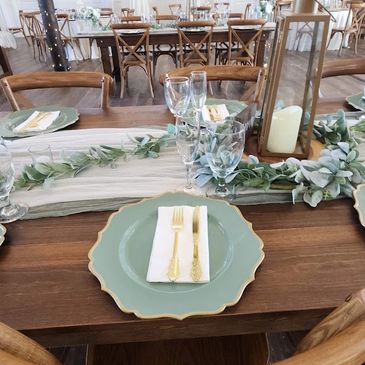 Elegant wedding table setting with green plates, gold cutlery, and leafy centerpiece.