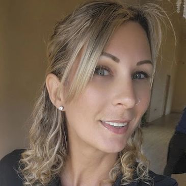 Woman with curly hair wearing a black polo shirt smiling indoors.