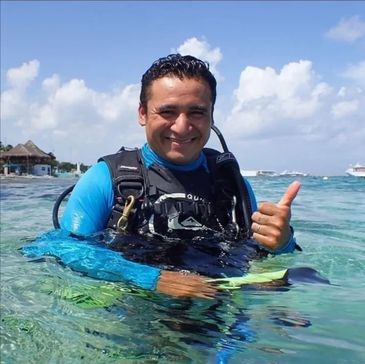 Smiling scuba diver giving a thumbs-up in clear ocean water.