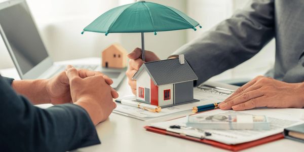 A person holds an umbrella over a model house during a business meeting.