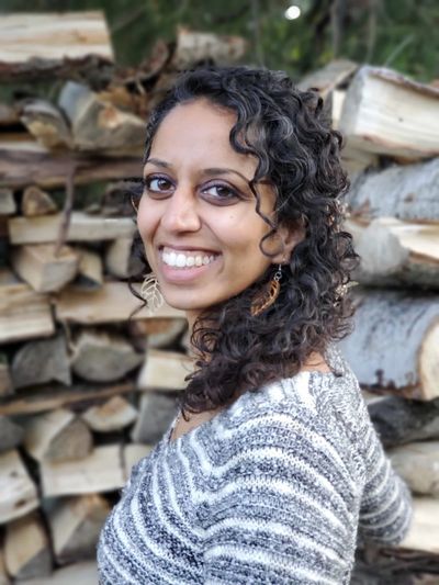 Smiling woman with curly hair in cozy sweater against stacked firewood.
