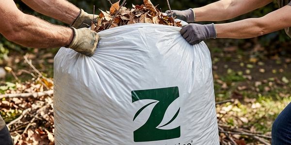 Two people holding a large white bag filled with dry leaves.