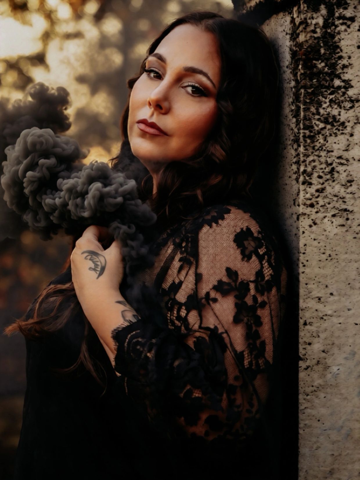 Woman in black lace holds black smoke, leaning against a textured wall.