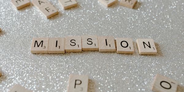 Scrabble tiles spell out the word 'MISSION' on a glittery surface.