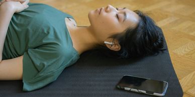 A woman lying on a mat with wireless earbuds and a phone nearby.