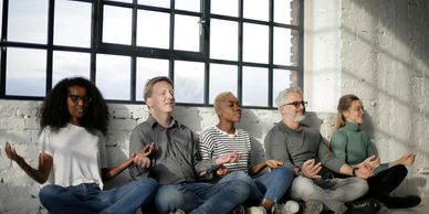 Diverse group meditating together indoors near large window.