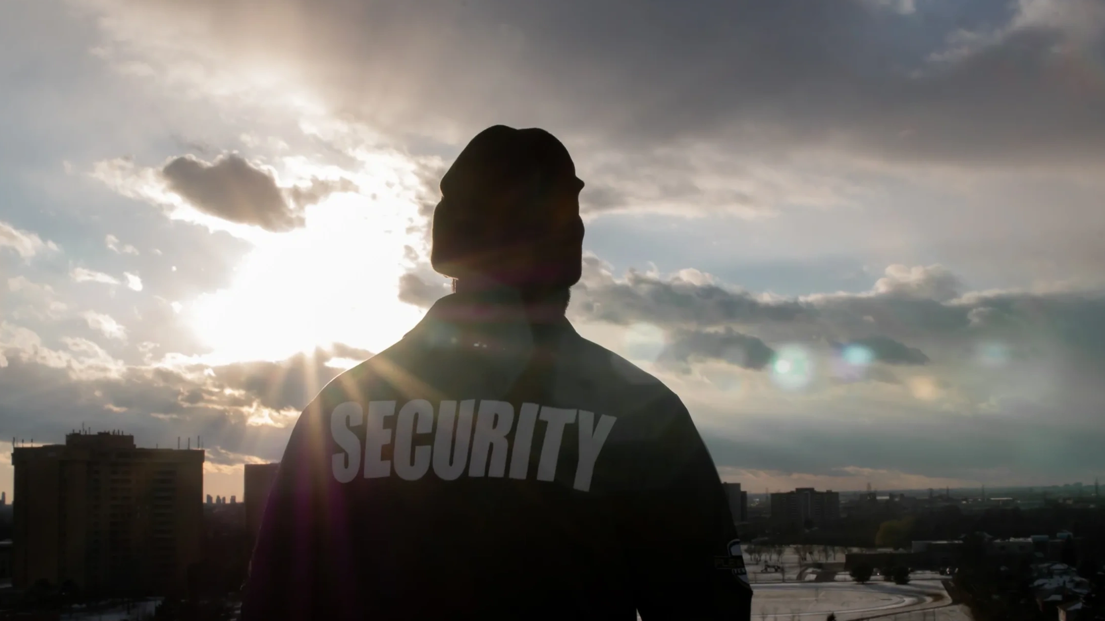 Silhouette of a security guard against a dramatic sunset sky in an urban setting.