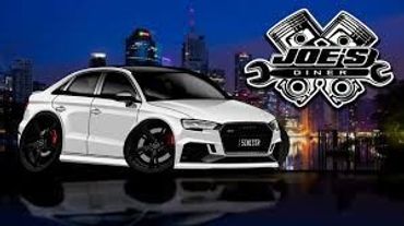 White Audi sedan with black rims in front of a cityscape at night.