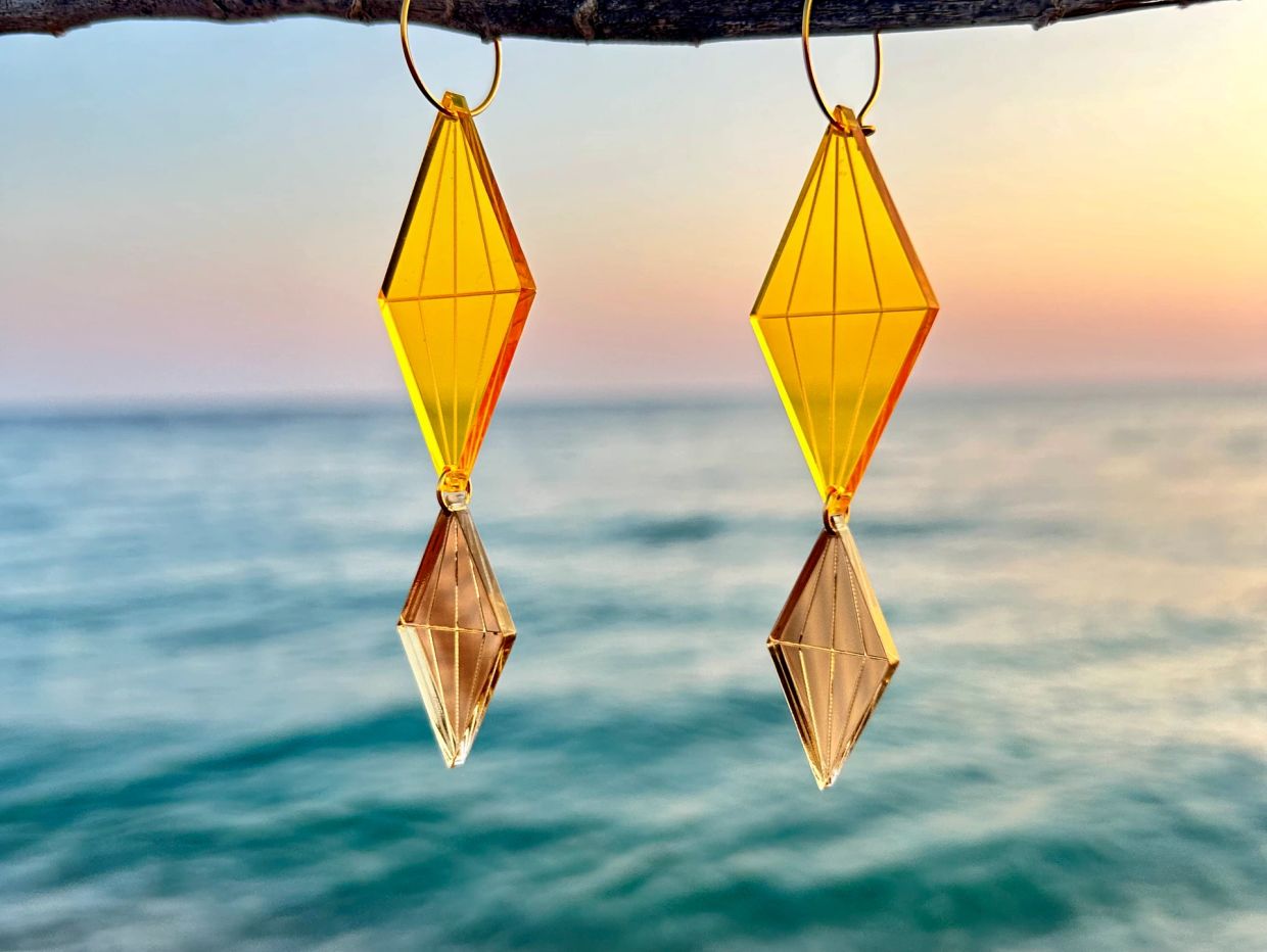 Pendientes geométricos colgando frente al mar al atardecer.