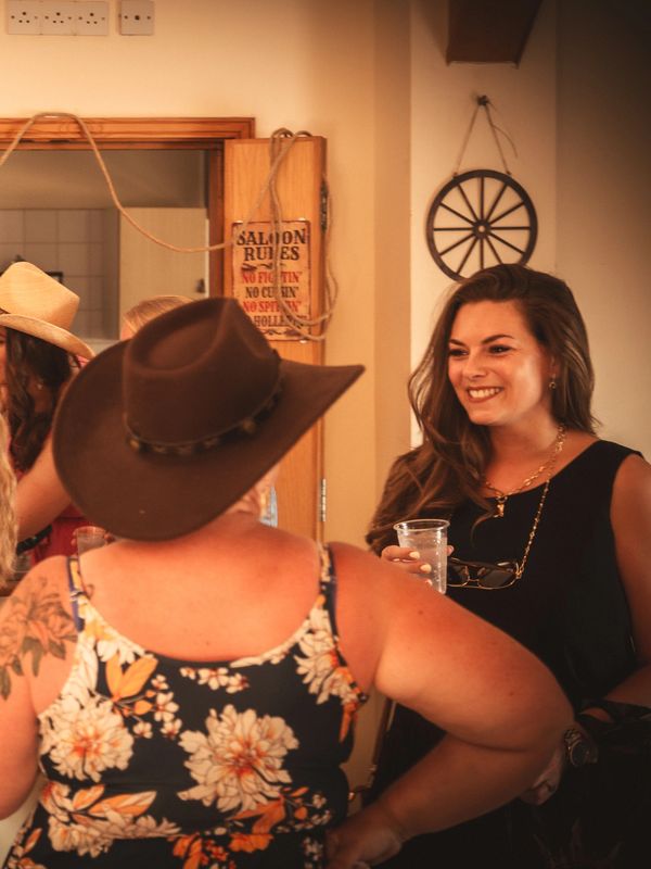 Women socializing indoors, one in a cowboy hat.