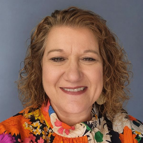 Smiling woman with curly hair wearing colorful floral top.