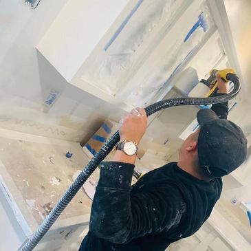 Worker using a power tool to sand a white surface in a room under renovation.