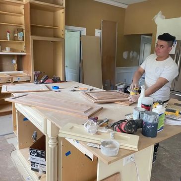 A man sanding wooden cabinet doors in a workshop.