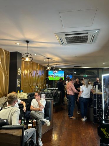 People socializing in a modern bar with leather seating and warm lighting.