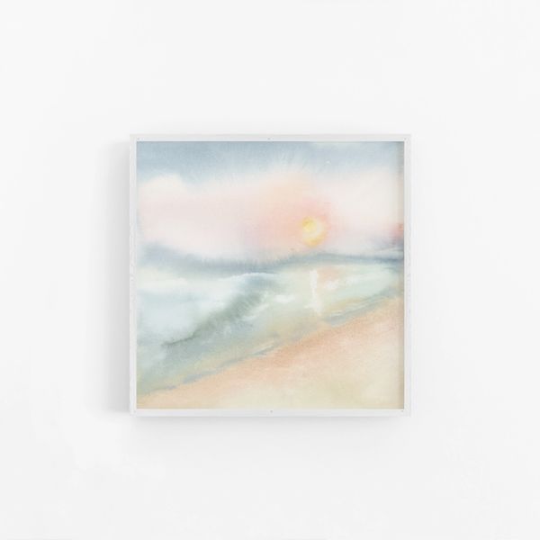 Sunset over a breach painted in light pastel watercolours framed as a print on a white wall.