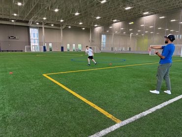 Man throwing ball to a boy running indoors on a turf field.