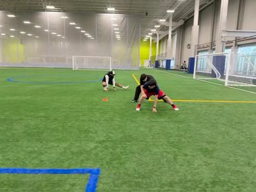 Two people stretching and training on an indoor sports field.