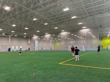 Indoor sports facility with kids playing on artificial turf field.