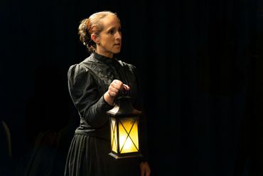 Woman in vintage black dress holding a glowing lantern in the dark.