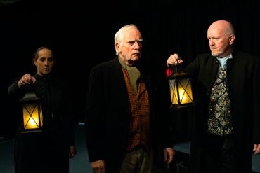 Three people in vintage attire holding lanterns in a dark setting.