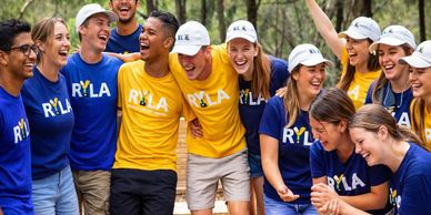 A diverse group of young people in RYLA shirts laughing and enjoying each other's company outdoors.