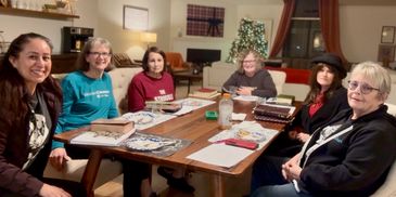 A group of six women sitting around a table with books and snacks during a cozy gathering.